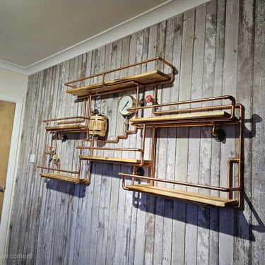 Steampunk industrial wall shelf with copper pipes, wood planks, and vintage gauges on rustic wall.
