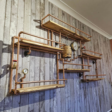 Handmade steampunk wall shelves with copper pipes, wood planks, gauges, and industrial decor elements.