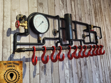 Handmade steampunk industrial coat rack with red hooks, gauge, and pipework on rustic wood wall
