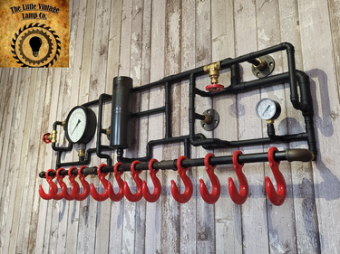 Industrial steampunk pipe coat rack with red hooks, pressure gauges, and wood wall backdrop