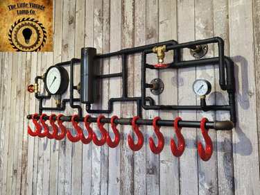 Industrial steampunk coat rack with red hooks, pressure gauges, and black metal piping on wood wall.