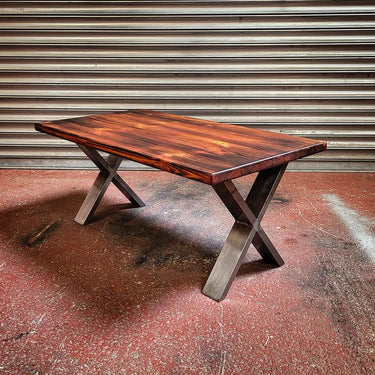 Industrial steampunk coffee table with wooden top and metal X-frame legs on red floor