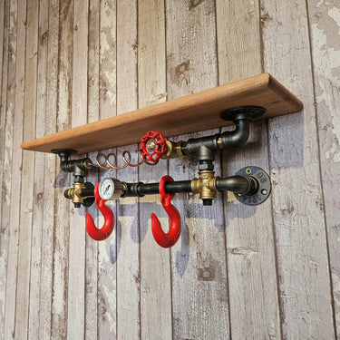 Steampunk industrial wall shelf with wood plank, metal pipes, red hooks, and gauge decor