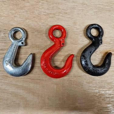 Three industrial metal lifting hooks in silver, red, and black on a wooden surface