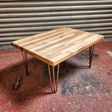 Industrial steampunk coffee table with wooden top and hairpin metal legs on a workshop floor.
