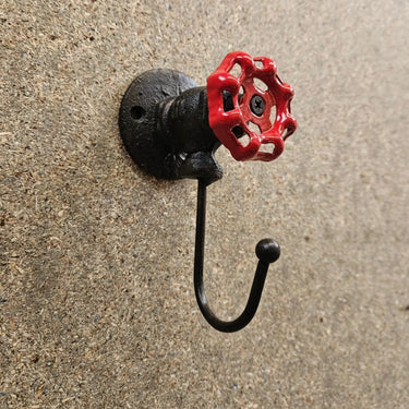Industrial steampunk wall hook with red valve handle on textured wall