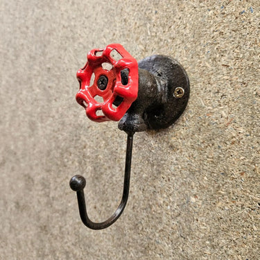 Industrial steampunk wall hook with red valve handle on rustic textured background