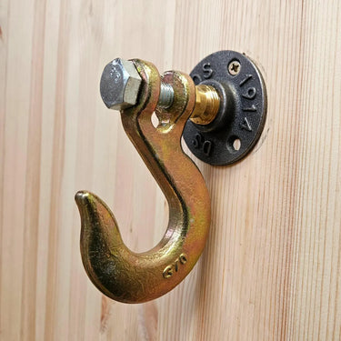 Industrial steampunk coat hook with metal flange mounted on light wood wall.
