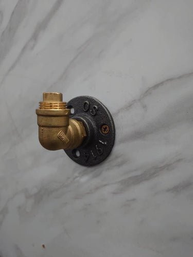 Industrial brass wall coat hook with flanged base on a marble surface