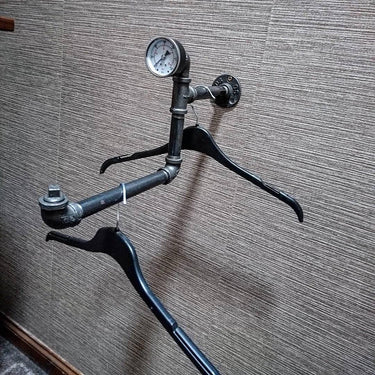 Wall-mounted industrial pipe clothes hanger rail with gauge and black hangers