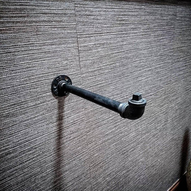 Wall-mounted industrial pipe clothes hanger rail on textured grey wall