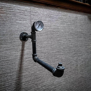 Industrial pipe clothes hanger rail with pressure gauge on textured wall