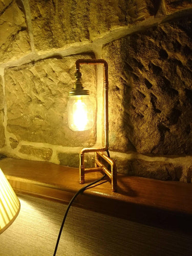 Industrial pipe table lamp with mason jar shade and Edison bulb against stone wall