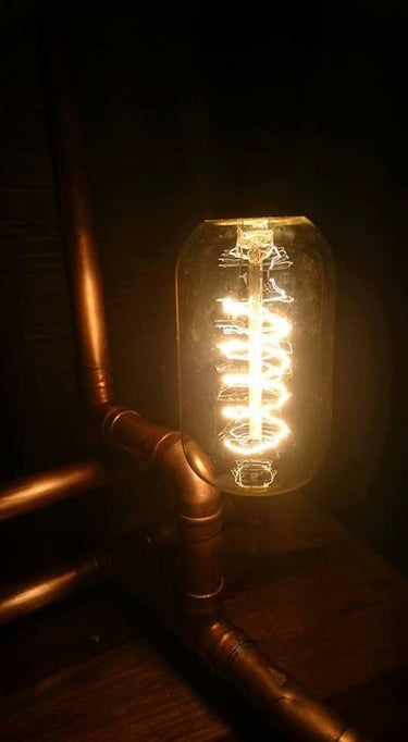 Industrial pipe table lamp with exposed vintage-style Edison bulb on wooden surface