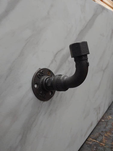 Industrial rustic coat hook made from black iron pipe on a marble wall