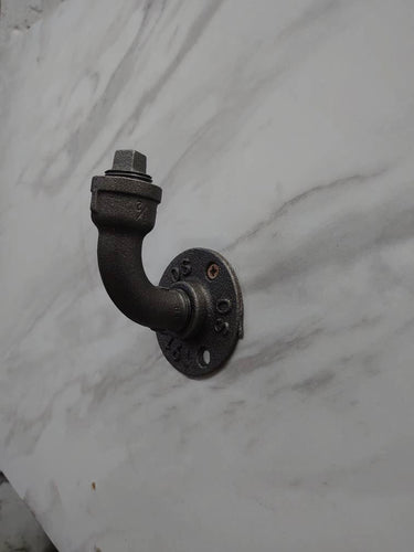 industrial steampunk coat hook made from black pipe, mounted on a marble wall