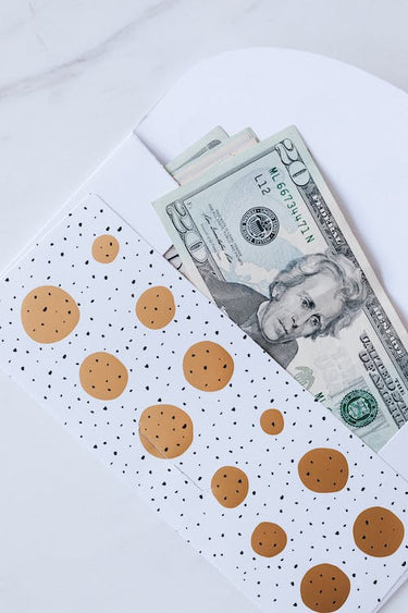 US twenty dollar bills in a white and gold polka dot envelope on a white surface