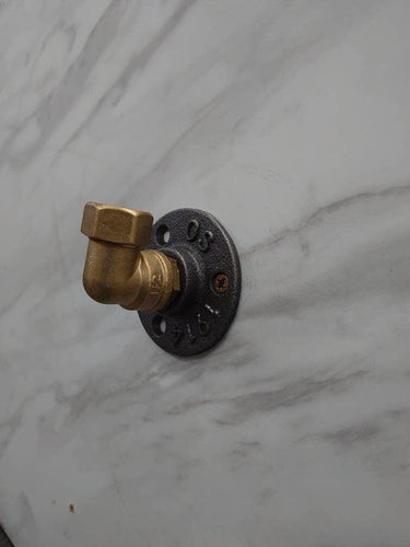 Retro industrial brass coat hook with black flange base mounted on a marble wall