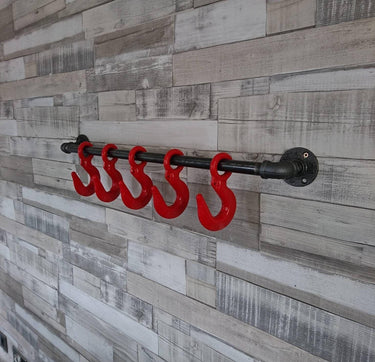 Industrial steampunk wall-mounted coat rack with red metal hooks on rustic wood panel wall