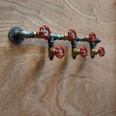 Steampunk industrial coat hooks made from metal pipes and red valve handles mounted on wood wall