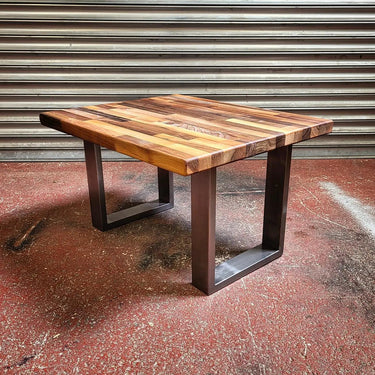 Industrial steampunk coffee table with wood block top and black metal legs on concrete floor