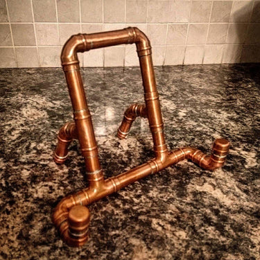 Steampunk industrial copper tablet stand made from pipe fittings on a marble countertop
