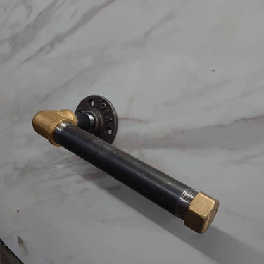 Steampunk brass and black metal pipe toilet paper holder mounted on marble wall.