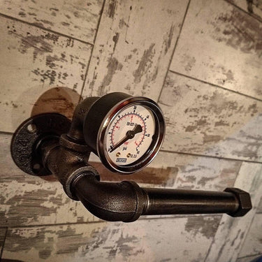 Steampunk pipe toilet paper holder with vintage steel gauge against rustic tiled wall