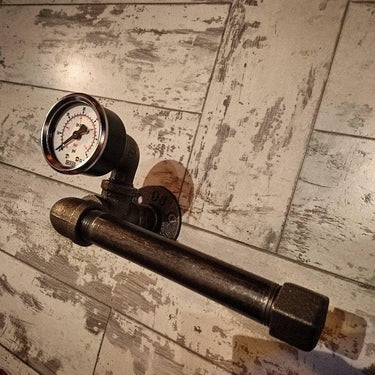 Steampunk industrial pipe toilet paper holder with steel pressure gauge on rustic wood wall.