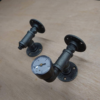Pair of industrial steampunk pipe wall brackets with gauge on wooden surface