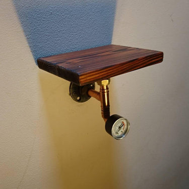 Steampunk wall shelf with dark wood plank, copper pipe, and industrial gauge on light wall
