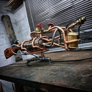 Steampunk industrial table lamp made from copper pipes, metal fittings, and wood, resembling a vintage tool, placed on a rustic workbench.