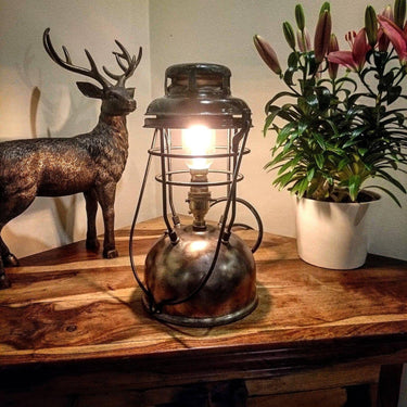 Vintage industrial table lamp with exposed bulb on wooden table, beside plant and deer sculpture