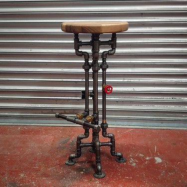 Industrial steampunk bar stool with metal pipe legs and wooden seat on a red floor