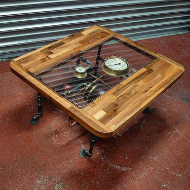 Steampunk coffee table with glass top, exposed gauges, wood frame, and industrial pipe legs