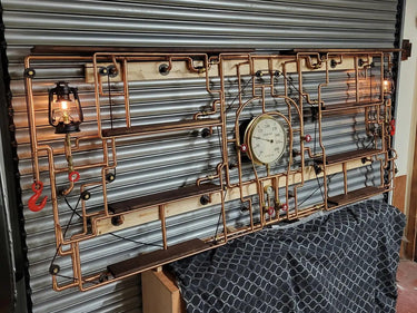 Steampunk industrial shelving unit with copper pipes, vintage gauge, lamps, and wood shelves