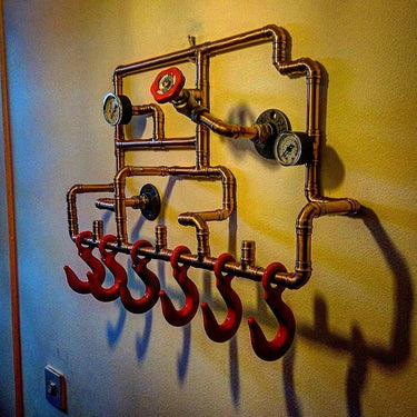 Steampunk coat rack made from copper pipes with vintage gauges and red industrial hooks on a wall