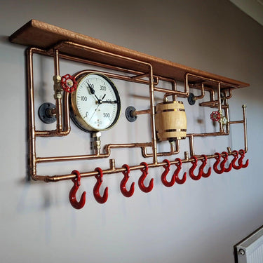 Steampunk industrial coat rack with copper pipes, red hooks, gauge, and wooden shelf