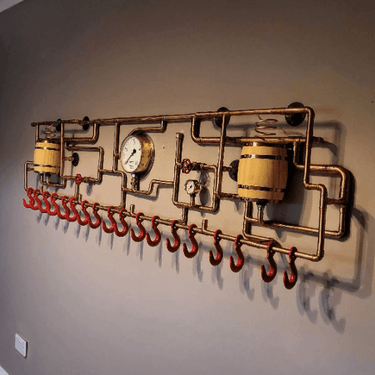 Industrial steampunk wall coat rack with copper pipes, red hooks, gauges, and barrel accents.