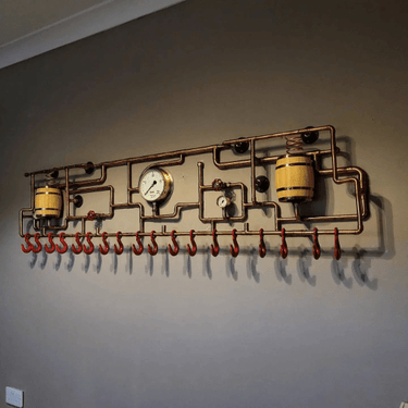 Steampunk coat rack with copper pipes, gauges, and red hooks mounted on a wall.