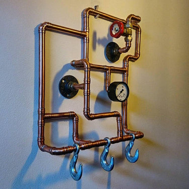 Steampunk coat rack made from copper pipes with industrial hooks, gauge, and valve wall-mounted.