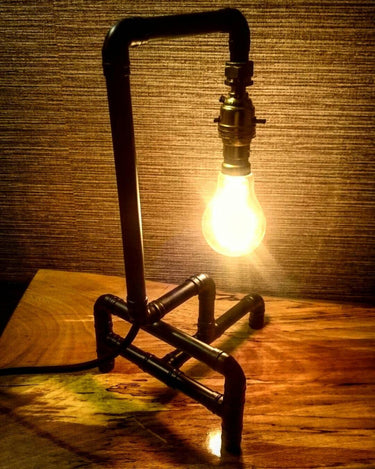 Industrial pipe table lamp with exposed bulb on wooden surface, steampunk lighting decor