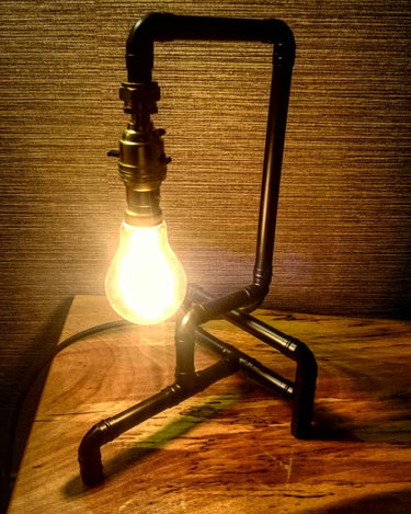 Industrial pipe-style table lamp with exposed bulb on a wooden surface