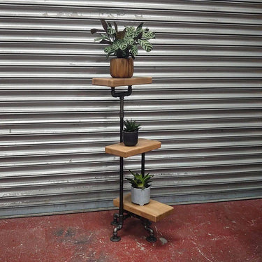 Steampunk industrial plant stand with three wooden shelves and metal pipe frame, holding potted plants.