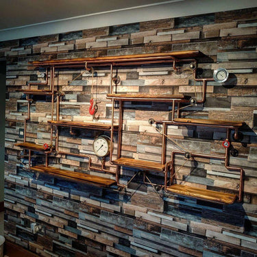 Steampunk industrial shelving unit with copper pipes, wood shelves, gauges, and pulleys on a rustic wall.