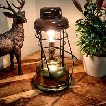 Vintage industrial table lamp with exposed bulb on wooden surface, next to deer figurine and plant.