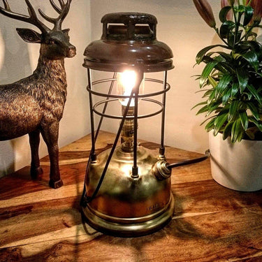 Vintage brass steampunk table lamp with exposed bulb on wooden surface, decor accents nearby
