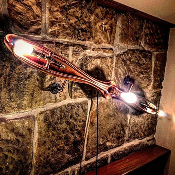 Steampunk propeller wall light with exposed bulbs and copper finish on stone wall