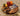 Round chunky walnut chopping board with two knives, vegetables, and citrus fruits on top