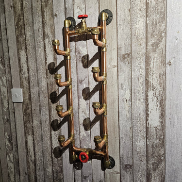 Industrial steampunk copper pipe wall shelf with brass fittings and red valve on rustic wood wall